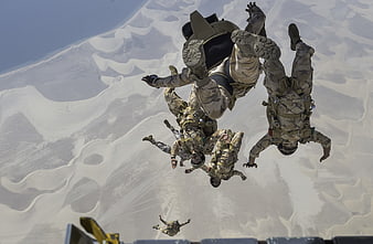 Military paratroopers skydiving over desert dunes
