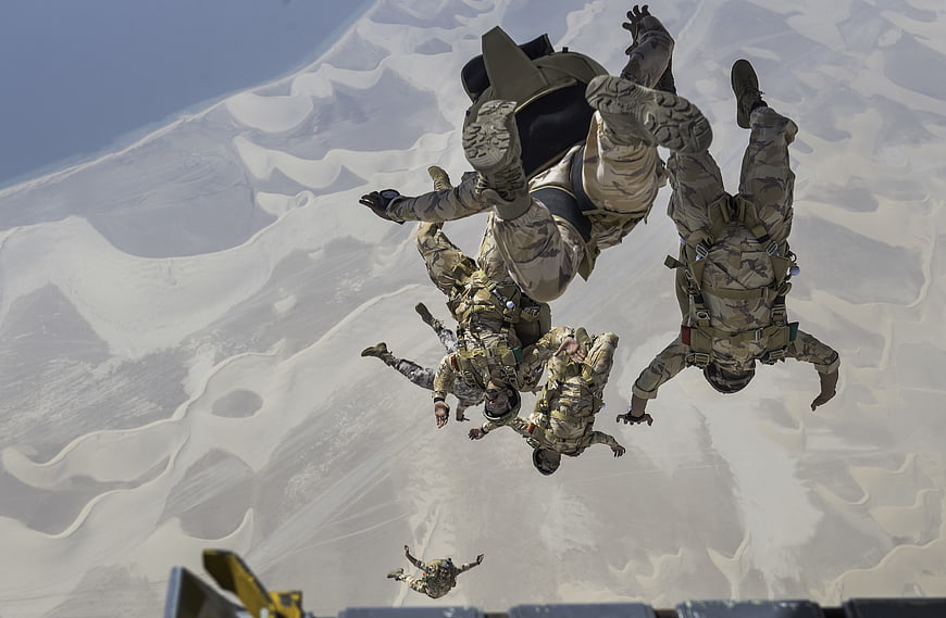 Military paratroopers skydiving over desert dunes