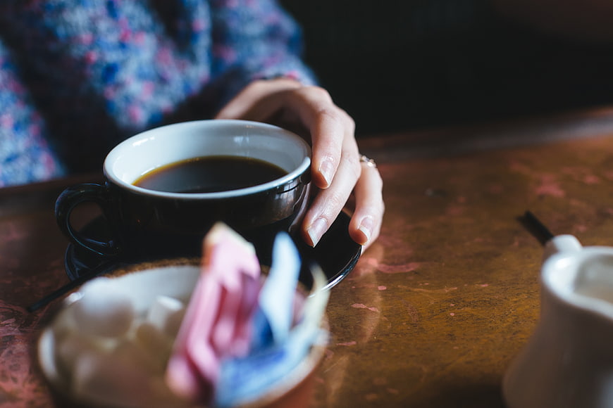 Woman's Hand Holding Black Coffee Cup on Wooden Table