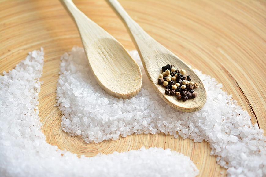 Coarse Sea Salt and Peppercorns in Wooden Spoons on Cutting Board