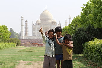 Three Indian boys posing with thumbs up in front of the Taj Mahal