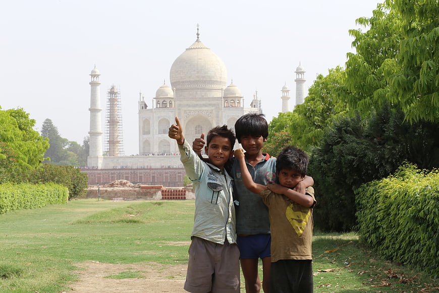 Three Indian boys posing with thumbs up in front of the Taj Mahal