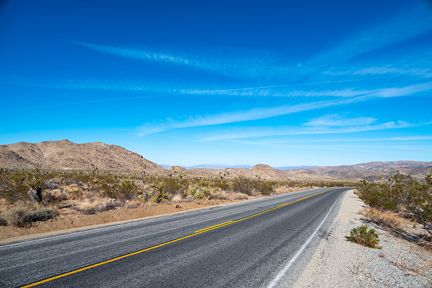 Empty Desert Highway Road with Joshua Trees and Blue Sky