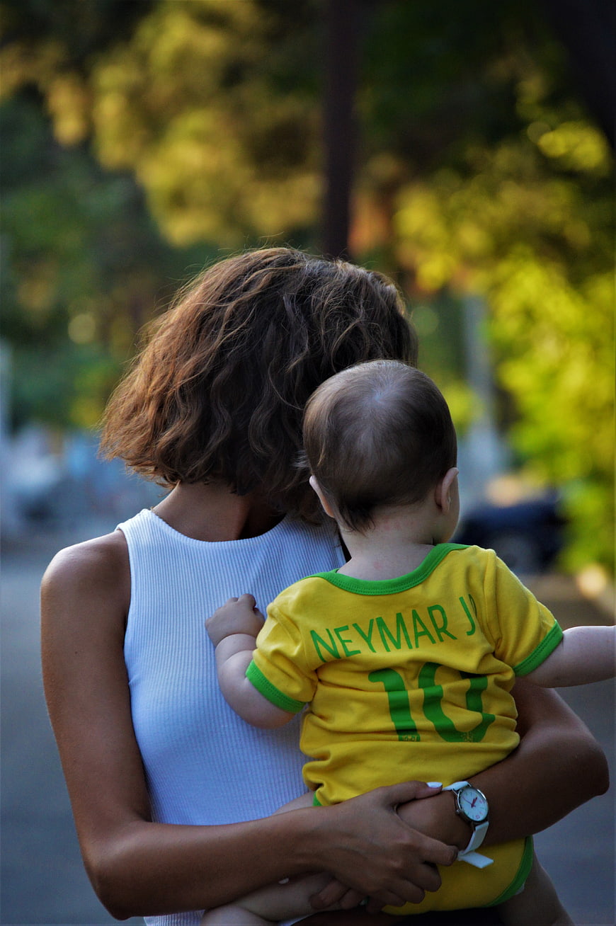 Mother holding baby in yellow Neymar soccer jersey outdoors