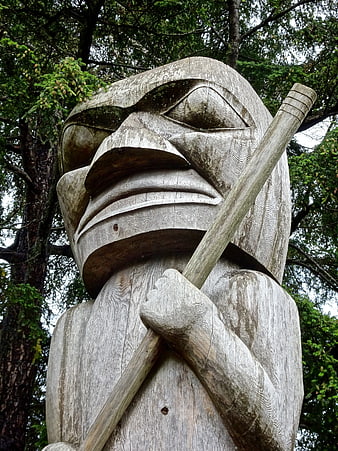 Weathered wooden totem pole figure holding a staff in a forest