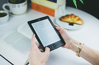 Hands holding e-reader with coffee and croissant on white table