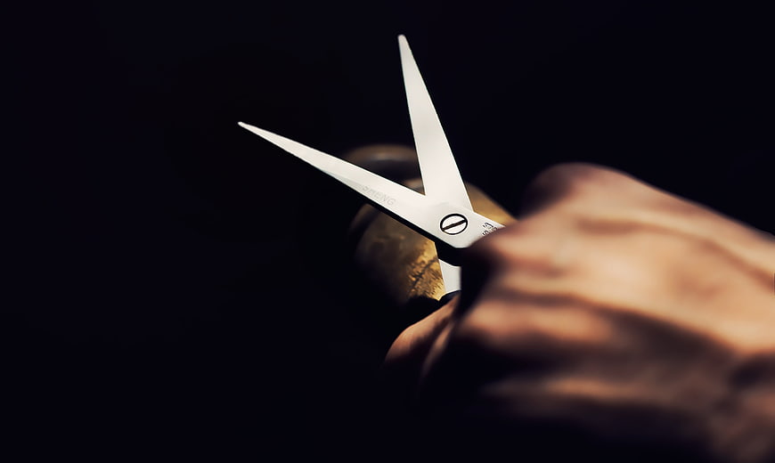 Close-up of hand holding silver scissors against dark background
