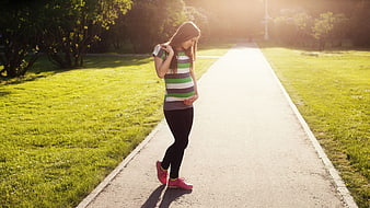 Pregnant woman walking on a park path in golden hour sunlight