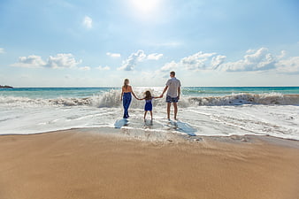 Family holding hands walking into ocean waves on sunny beach