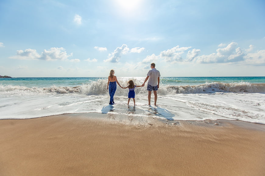 Family holding hands walking into ocean waves on sunny beach
