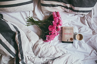 Pink peonies, book, and coffee on messy white bed sheets