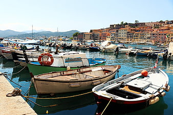Colorful boats docked in a Mediterranean harbor with coastal town