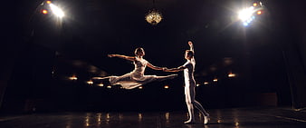 Ballet dancers performing dramatic leap on dark stage