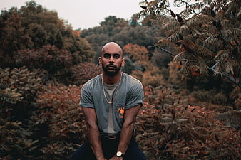 Portrait of bald man in grey t-shirt sitting in autumn forest