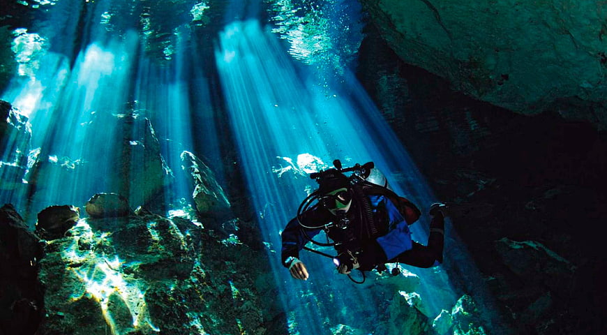 Scuba Diver Swimming Through Sunbeams In A Deep Blue Cenote