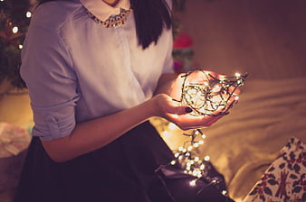 Woman holding glowing Christmas lights in hands