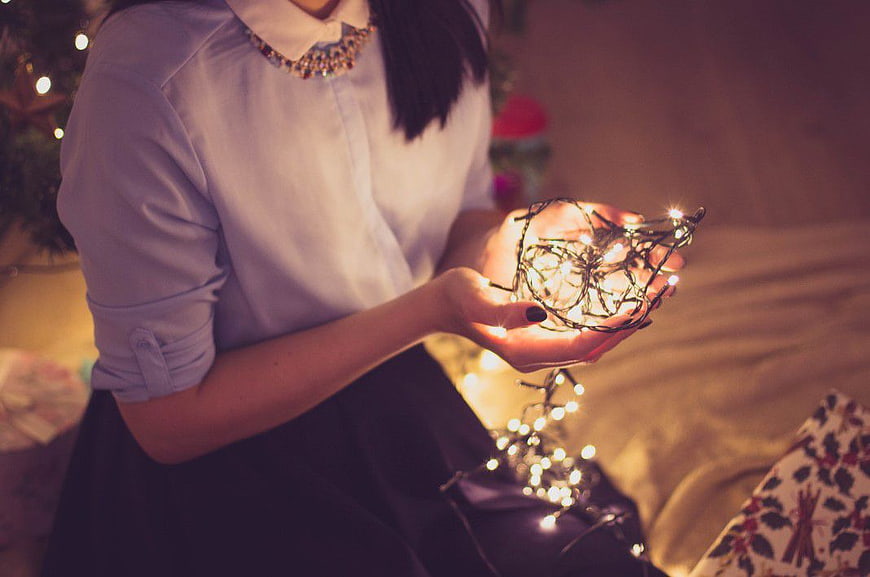 Woman holding glowing Christmas lights in hands