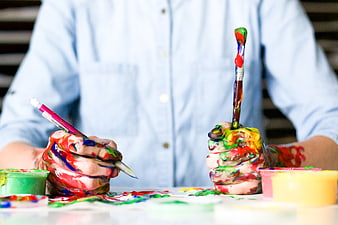 Close-up of artist hands covered in colorful paint holding brushes