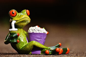 Cute ceramic frog figurine relaxing with popcorn and drink