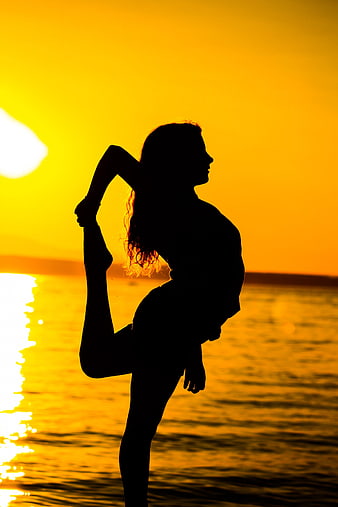 Silhouette of woman doing yoga pose on beach at sunset