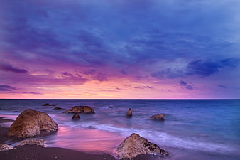 Dramatic purple and pink sunset over rocky ocean beach