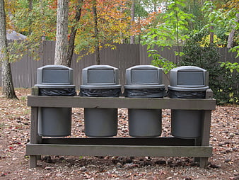 Four gray trash cans in wooden rack outdoors
