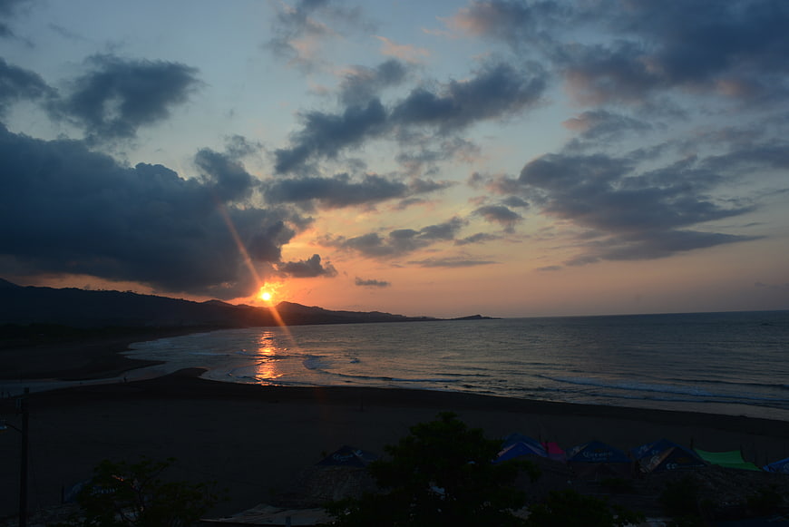 Dramatic Sunset Over Beach with Tents and Mountains