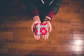 Hands holding small red gift box on wooden floor