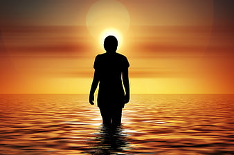Silhouette of woman standing in ocean at sunset