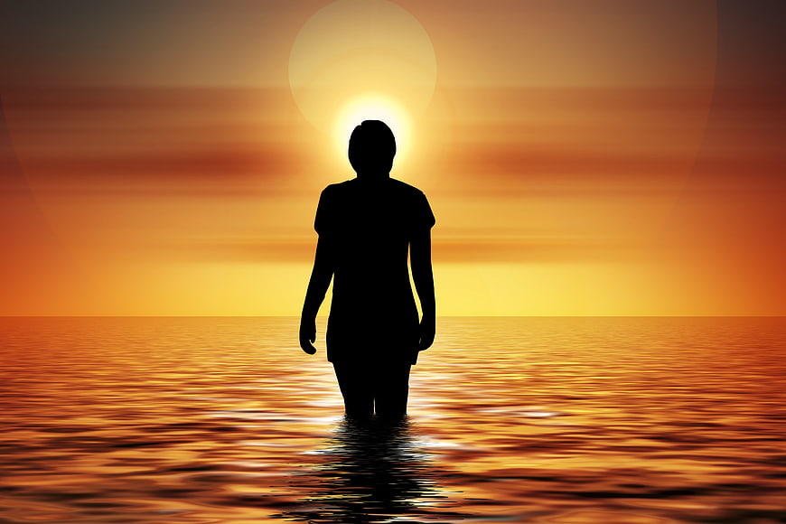 Silhouette of woman standing in ocean at sunset
