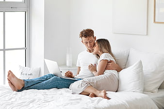 Young couple relaxing on bed with laptop in bright bedroom