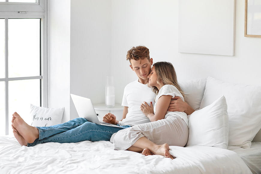 Young couple relaxing on bed with laptop in bright bedroom