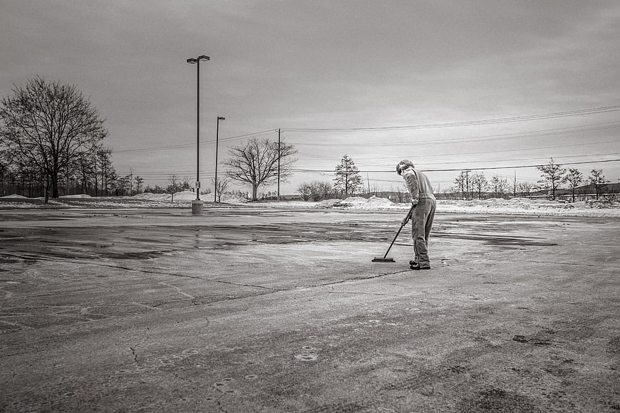 Man Sweeping Wet Concrete Parking Lot in Winter