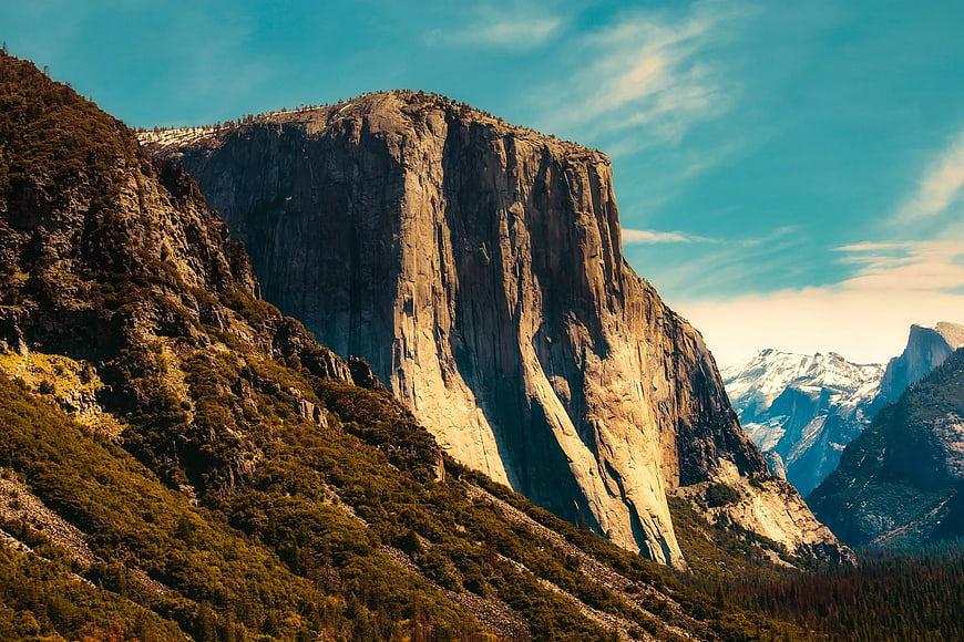 Majestic granite mountain peak with forested slopes and blue sky