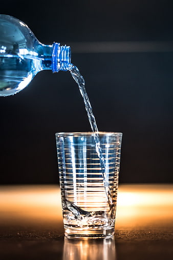 Water Pouring From Blue Bottle Into Ribbed Glass On Dark Background