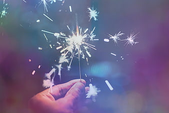 Hand holding sparkler with colorful bokeh background