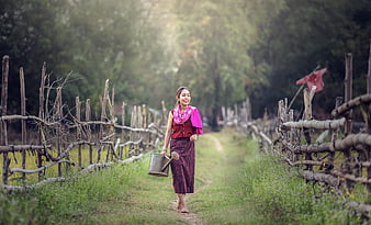 Asian woman walking in rural village with watering can