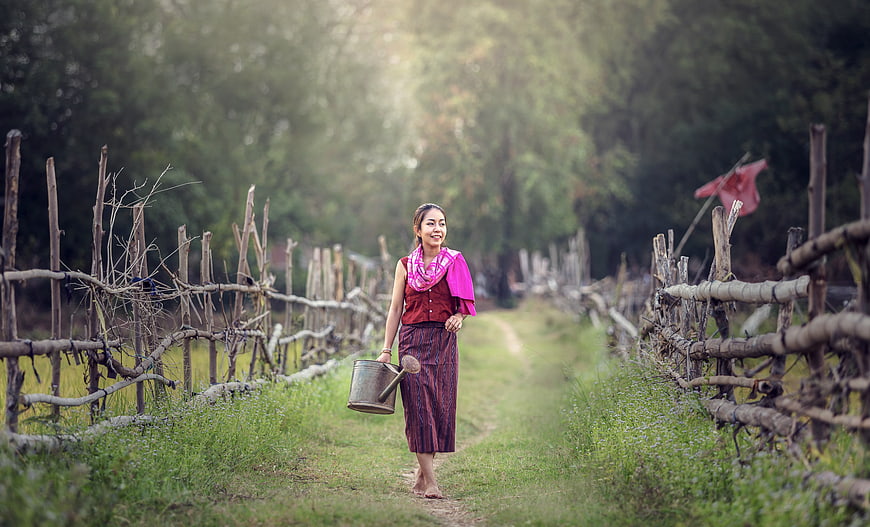 Asian woman walking in rural village with watering can