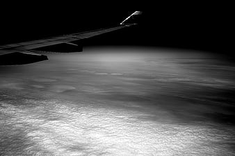 Airplane wing silhouette over clouds at night in black and white