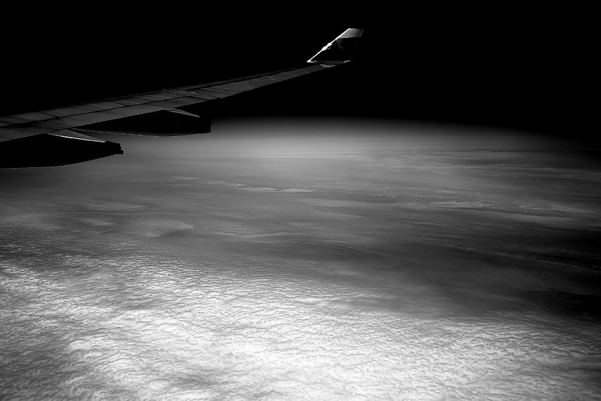 Airplane wing silhouette over clouds at night in black and white