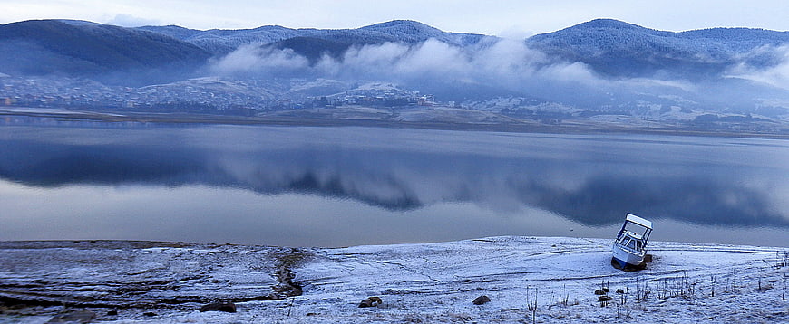 Panoramic winter landscape with boat on frozen lake shore