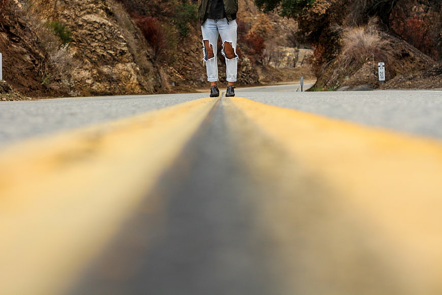 Person Walking on Yellow Road Lines in Nature