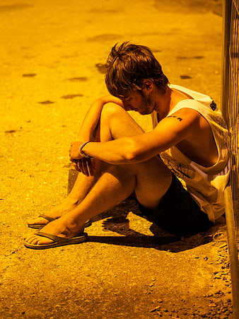 Young man sitting alone on pavement at night in yellow light