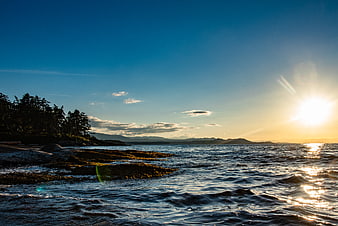 Sunset over rocky coastline with forest and mountains