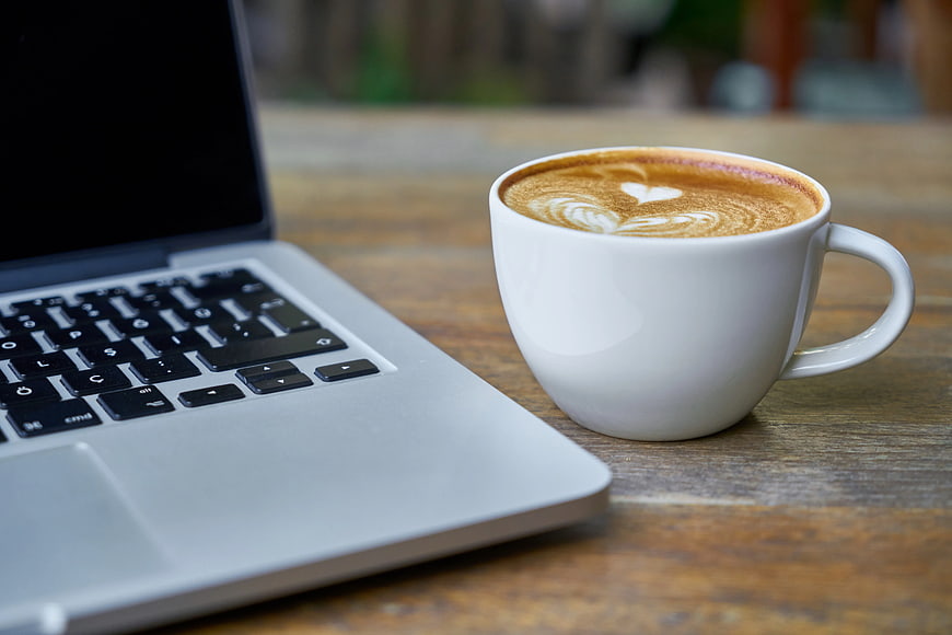 Latte with Heart Art Next to Laptop on Wooden Table