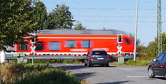 Fast red train speeding past railroad crossing with waiting cars