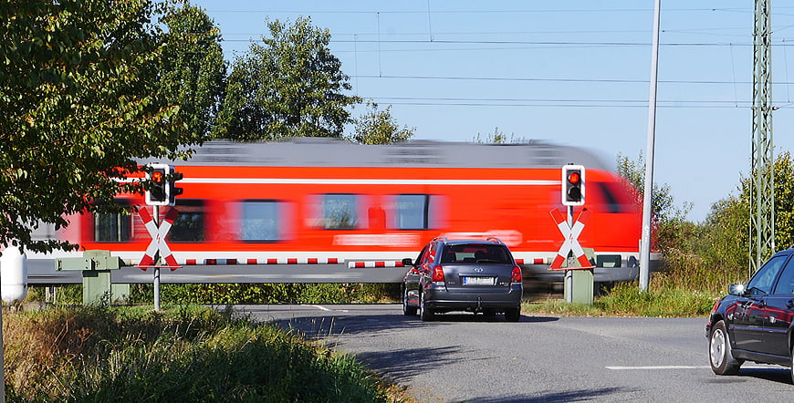 Fast red train speeding past railroad crossing with waiting cars