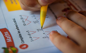 Close-up of child writing math homework with yellow pen