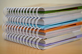 Stack of colorful spiral notebooks on wooden desk