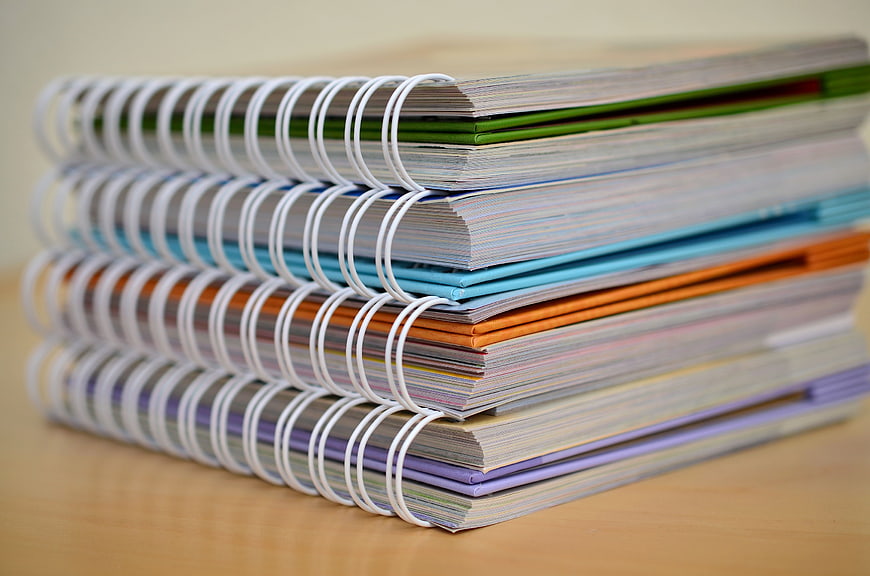 Stack of colorful spiral notebooks on wooden desk